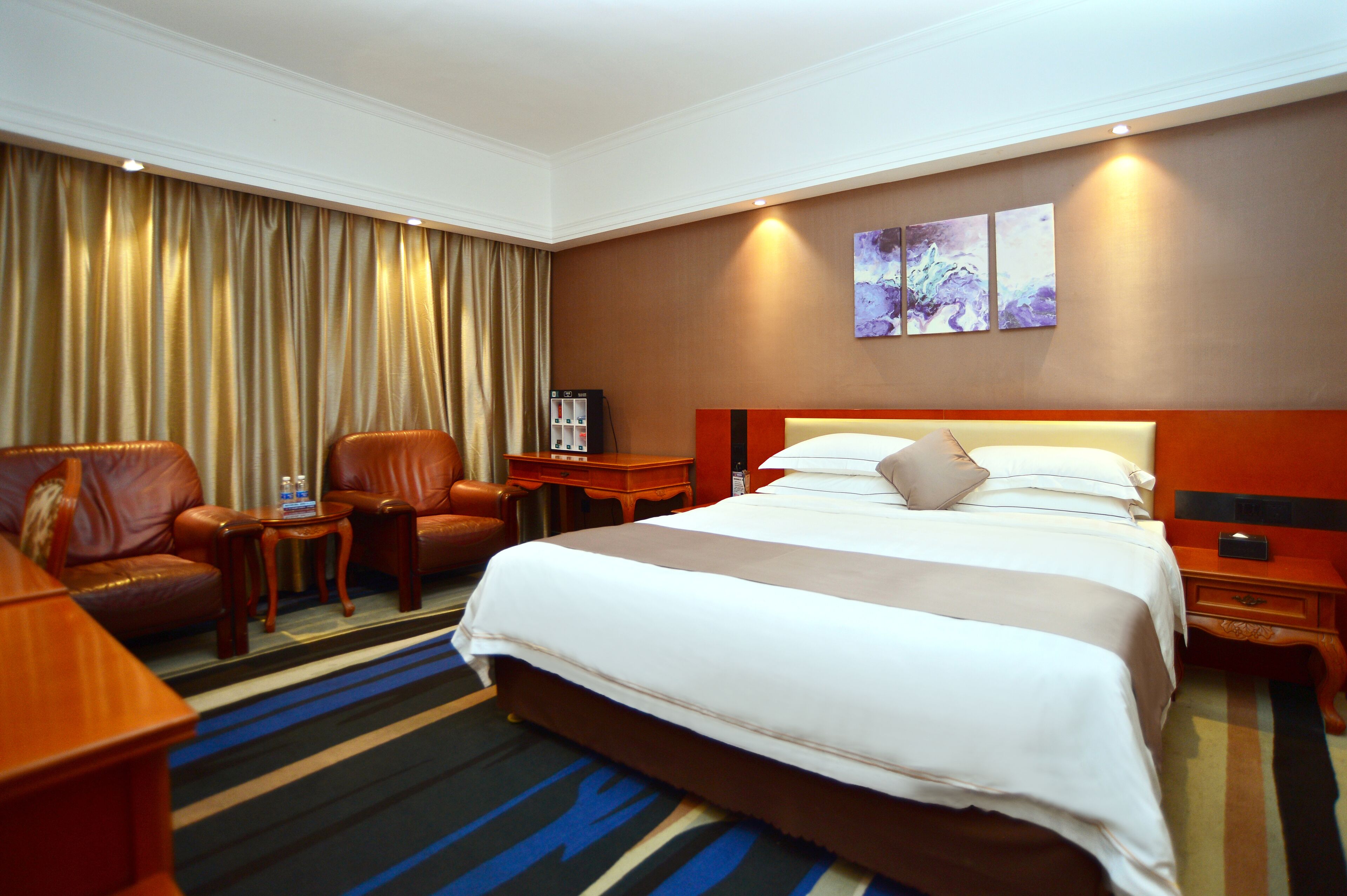 A hotel room with a large bed, a sofa, a chair, a nightstand, and a small table.
