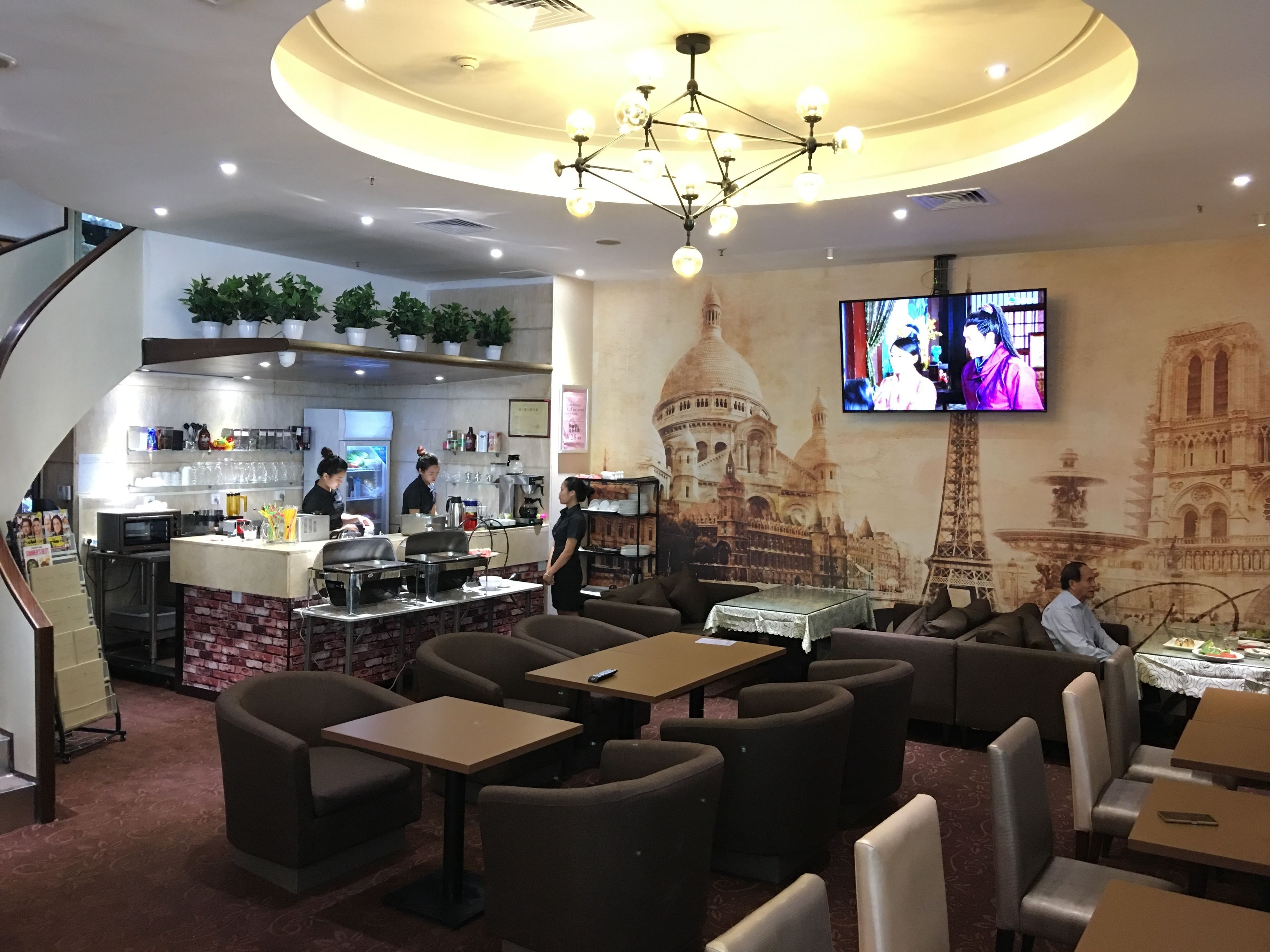 A restaurant with a central bar, seating area, and a large TV screen.