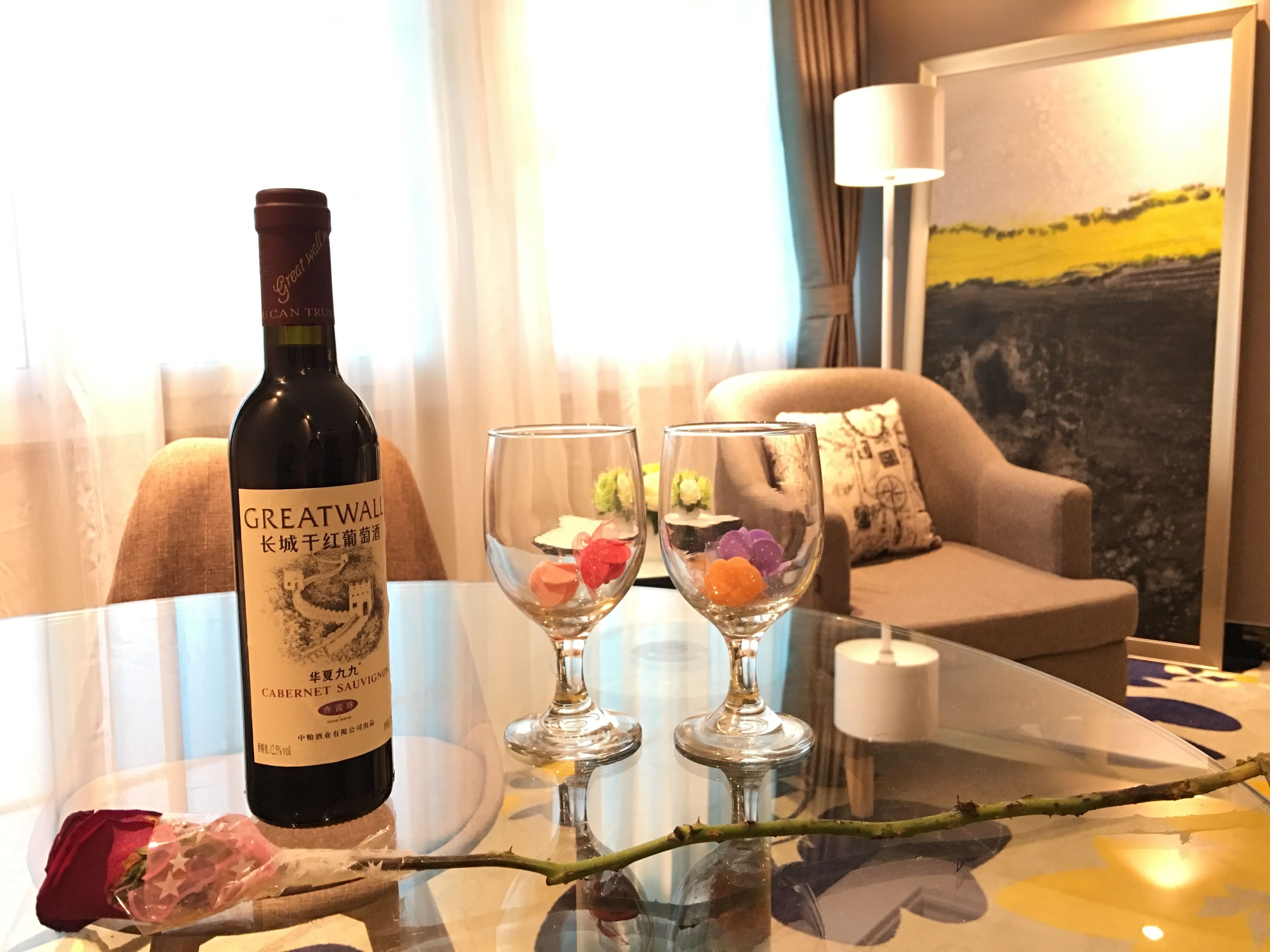 Una botella de Cabernet Sauvignon Great Wall sobre una mesa con dos copas de vino que contienen decoraciones coloridas.