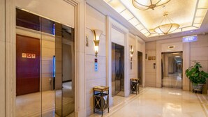 Un vestíbulo de hotel con ascensores, apliques de pared y una planta en maceta.