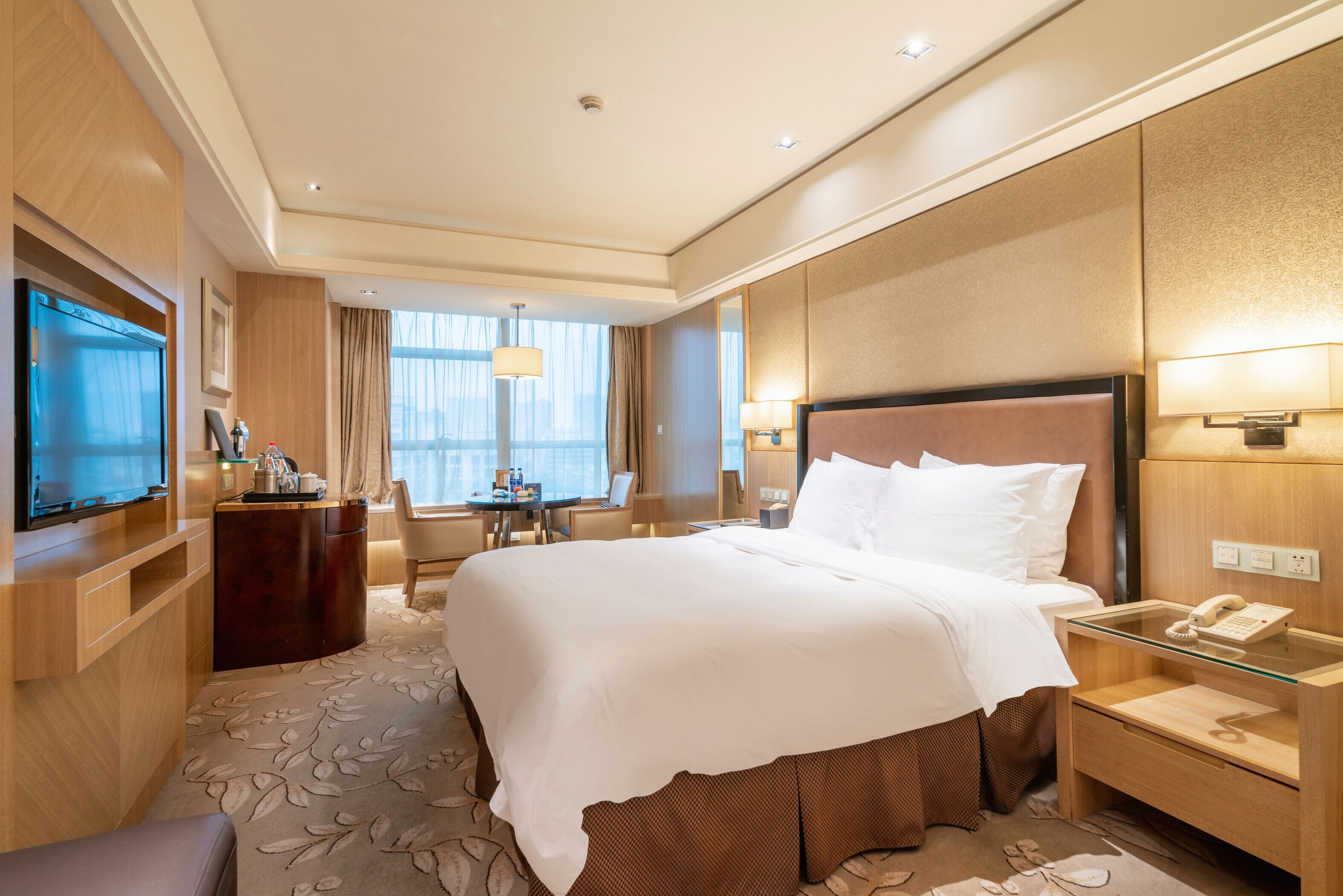 Ein Hotelzimmer mit einem großen Bett, einem Schreibtisch mit Computer, einem Fernseher und einem Telefon.