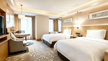 A hotel room with two beds, a desk, a chair, a television, and a large window.