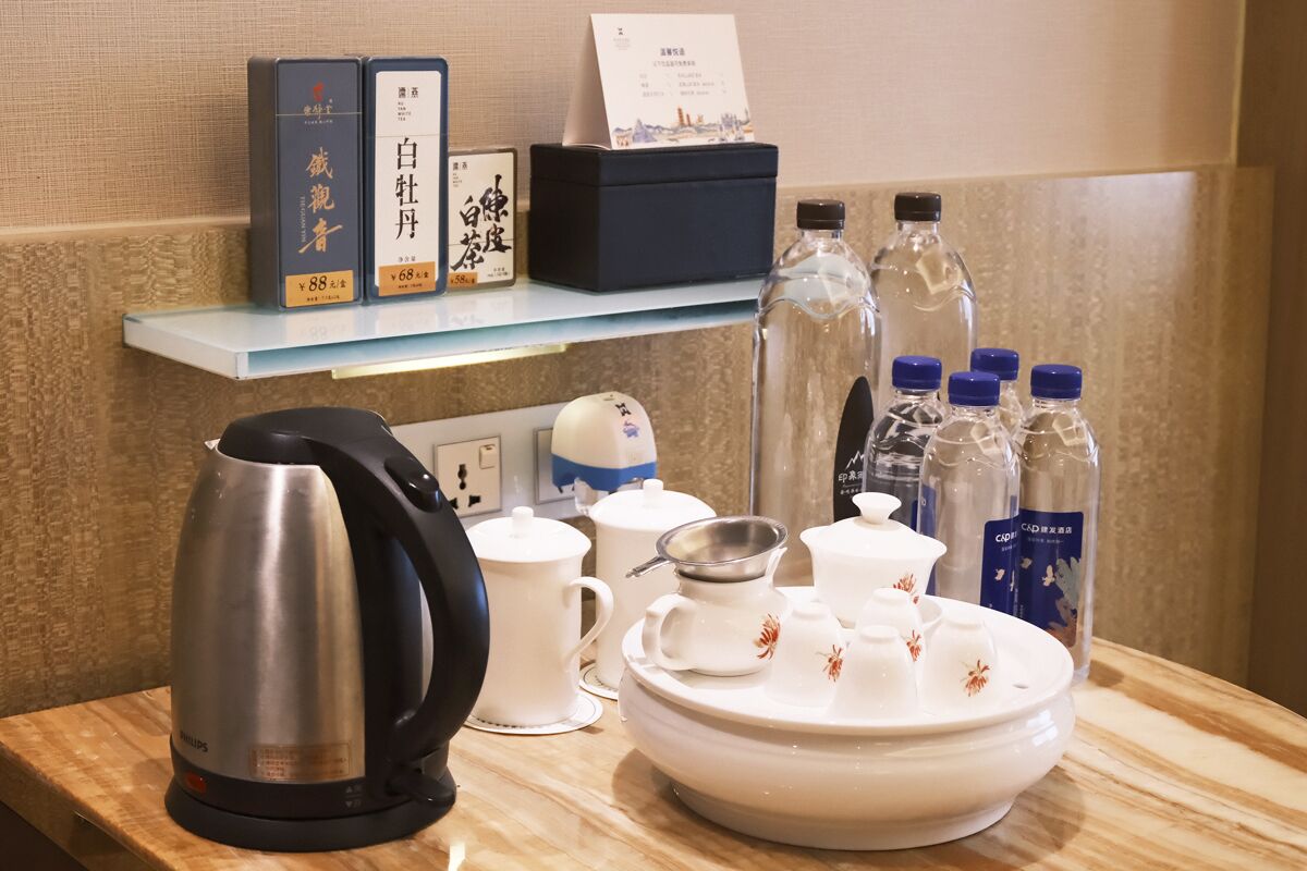 Preparación para el desayuno en una habitación de hotel, con hervidor, tetera, tazas, una bandeja con servicio de té y botellas de agua.