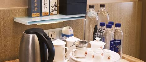 Preparación para el desayuno en una habitación de hotel, con hervidor, tetera, tazas, una bandeja con servicio de té y botellas de agua.