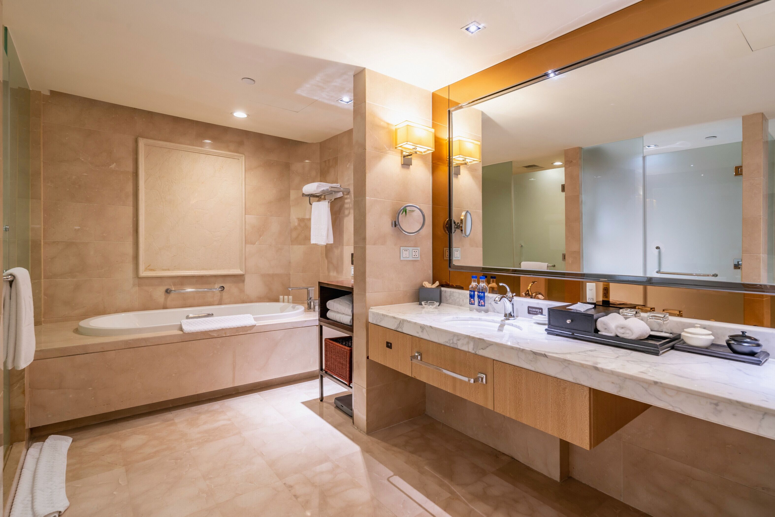 Un baño moderno con un espejo grande, una bañera, un lavabo y un mueble de tocador con artículos de aseo.