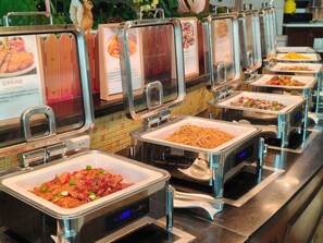 Un bufé con diversas opciones de comida, incluyendo un plato con pollo y vegetales, y un reloj digital mostrando la hora.