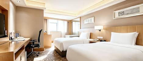 A hotel room with two beds, a desk, a chair, a TV, and a window with curtains.
