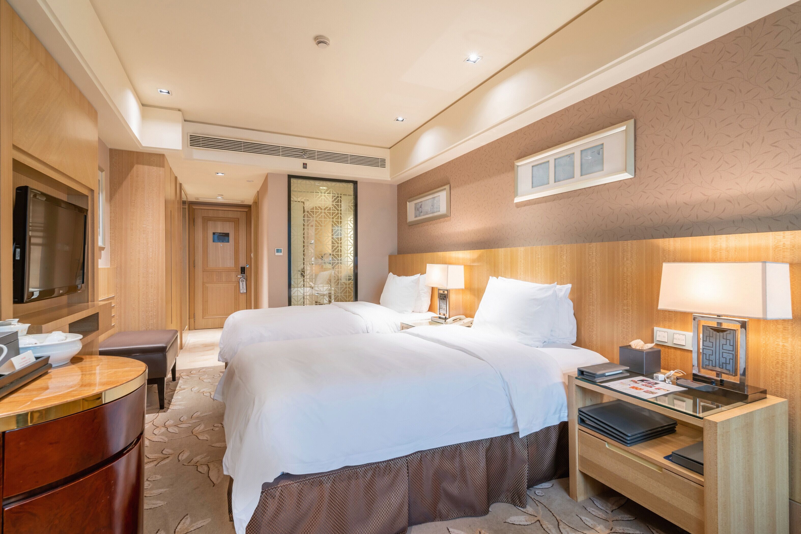 Una habitación de hotel con cama, mesitas de noche, televisión y escritorio con lámpara.
