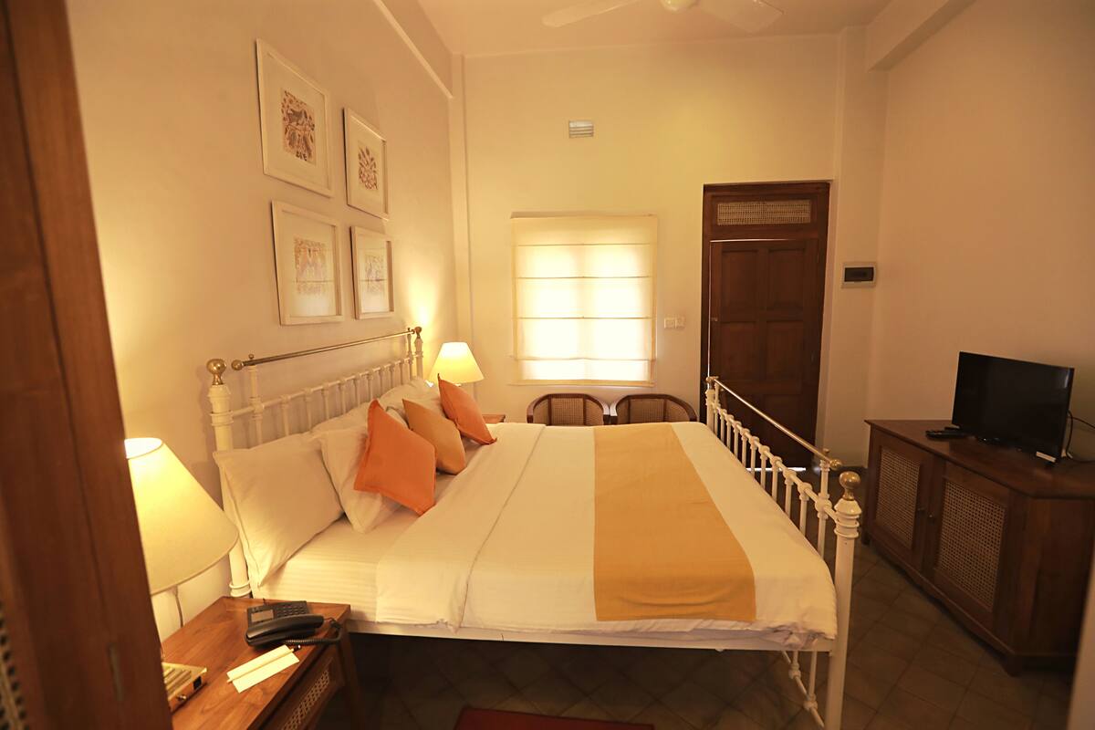 Habitación de hotel ordenada con cama, lámparas de noche, televisor y ventana con persianas.
