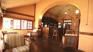 A cozy bar area with wooden furniture, a bar counter, and a view of the outside through large windows. - Bandarawela Hotel (Bandarawela)