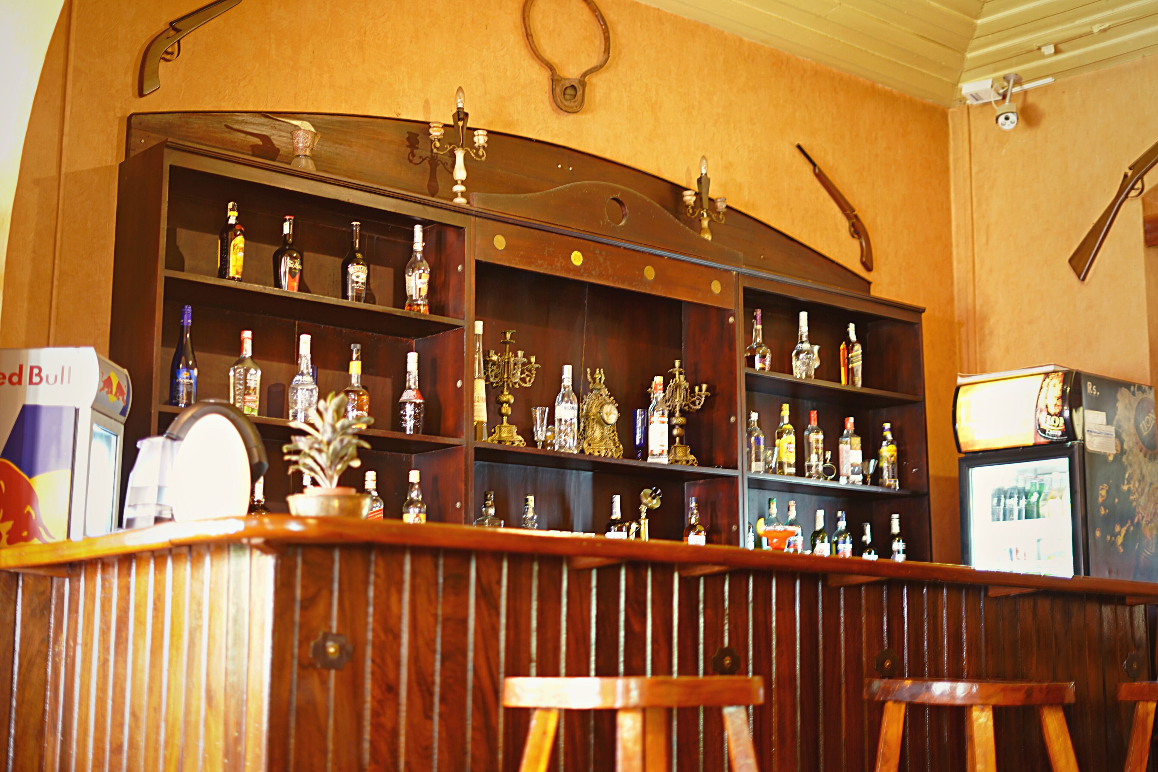 Een bar met houten planken vol flessen, een bar in vintage-stijl en twee houten krukken.