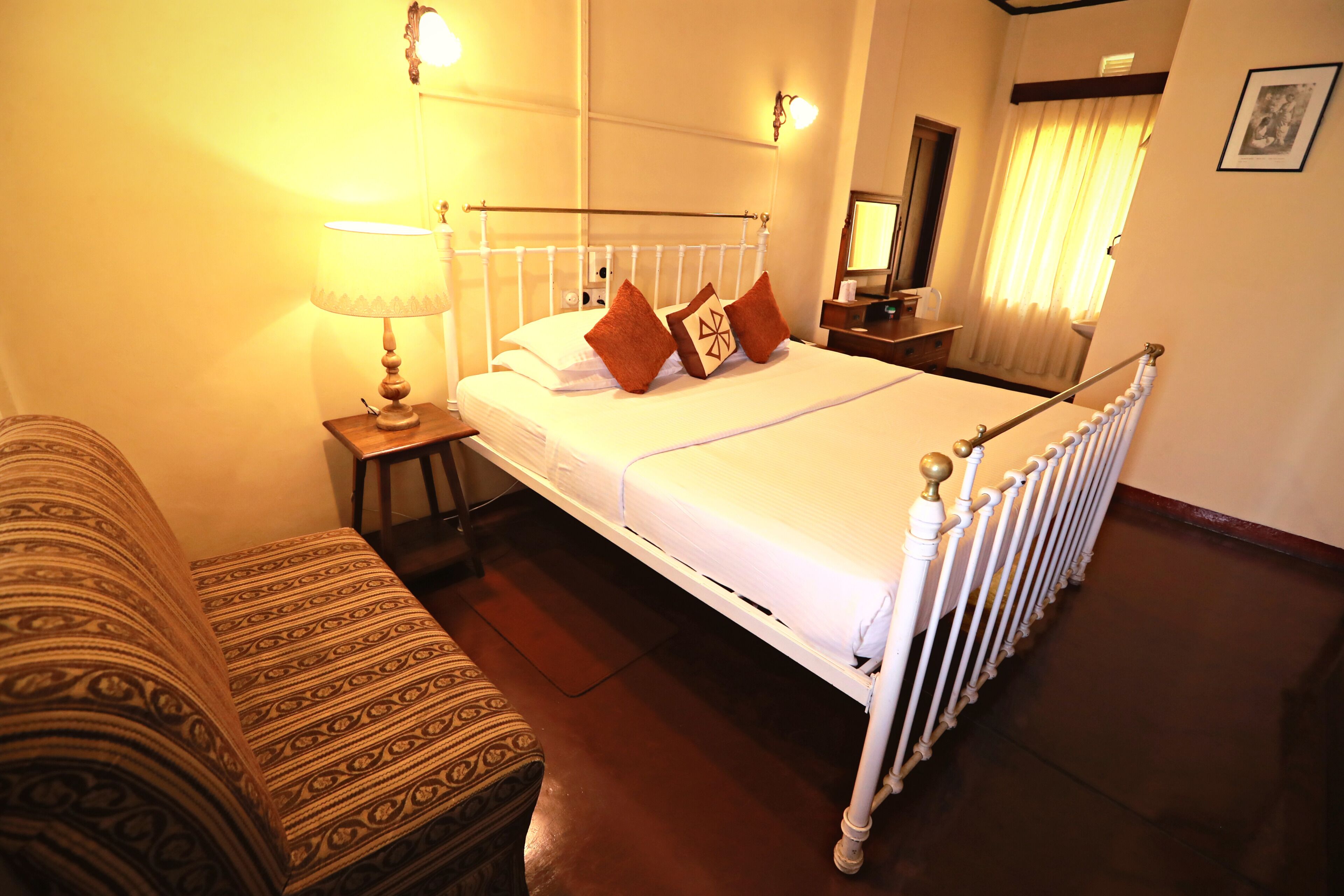 Une chambre d’hôtel bien rangée, avec un lit, une table de chevet, une lampe et un canapé à motifs.