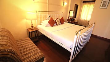 Quarto de hotel bem arrumado com cama, mesa de cabeceira, abajur e um sofá estampado.