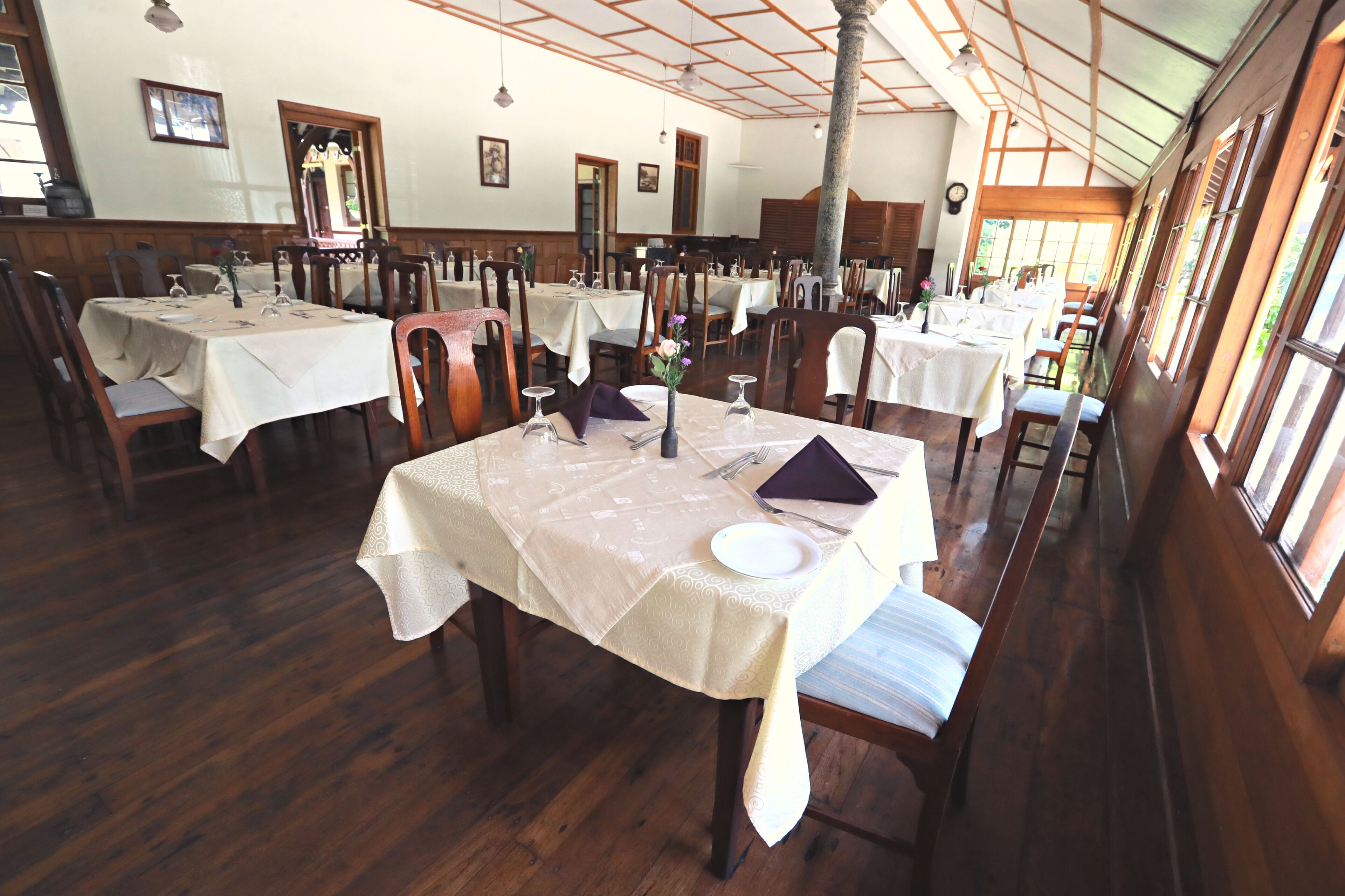 A restaurant with multiple tables set for dining, wooden chairs, and a high ceiling with wooden beams.