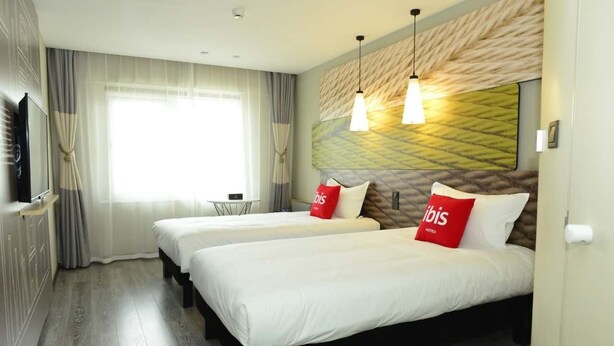 Habitación de hotel con dos camas, televisión y ventana con cortinas.