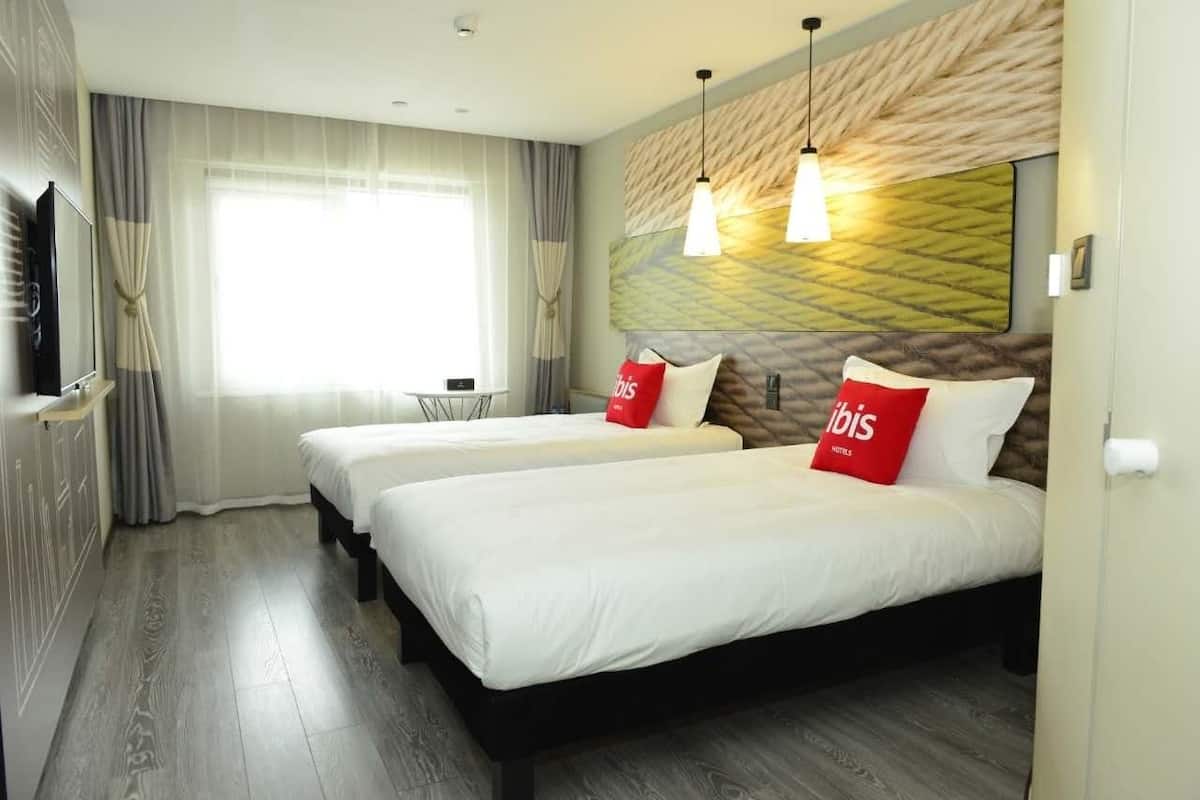 Habitación de hotel con dos camas, televisión y ventana con cortinas.
