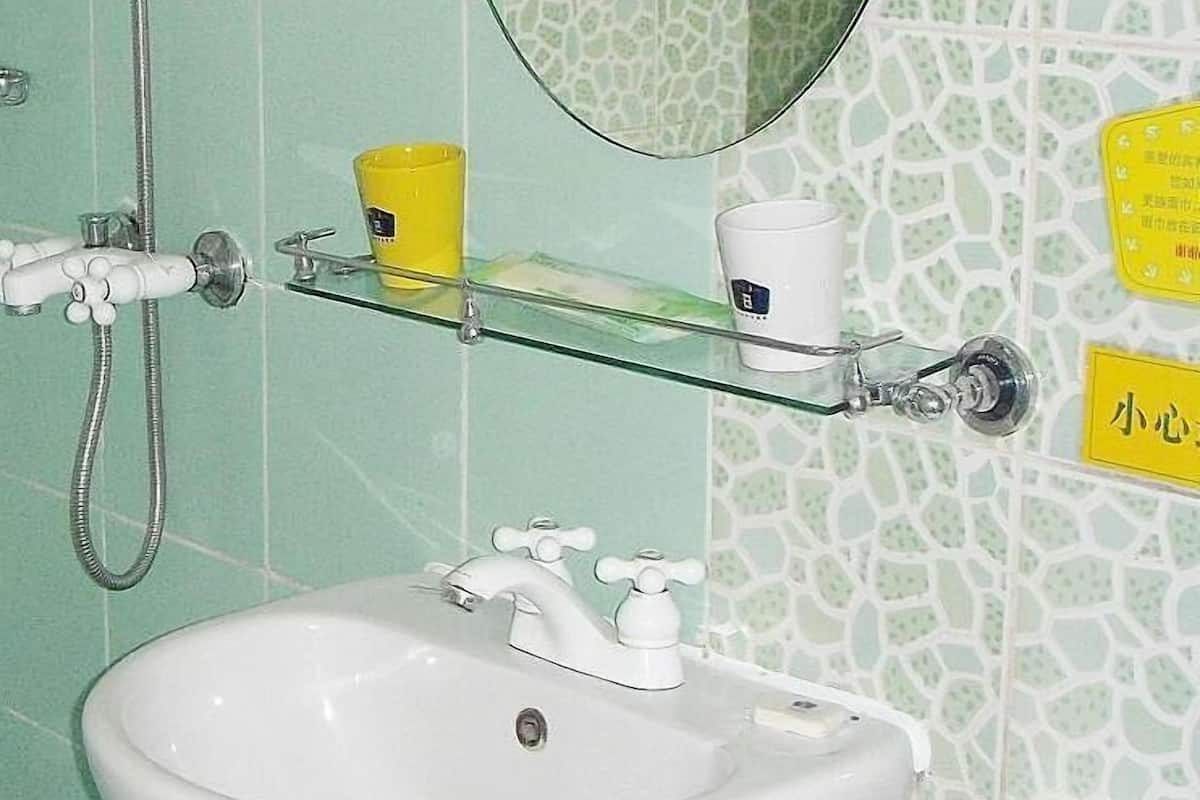 Un baño con un lavamanos blanco, un estante de vidrio con artículos de aseo, una ducha con cabezal de ducha manual y un espejo con marco redondo.