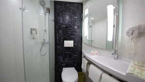 Un baño con cabina de ducha de vidrio, inodoro, lavamanos con espejo y secador de pelo.