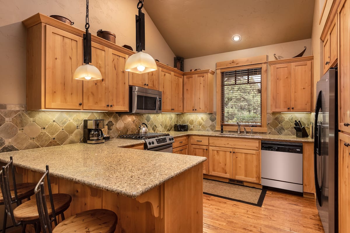 A kitchen with wooden cabinets, granite countertops, stainless steel appliances, and a large island with bar stools.