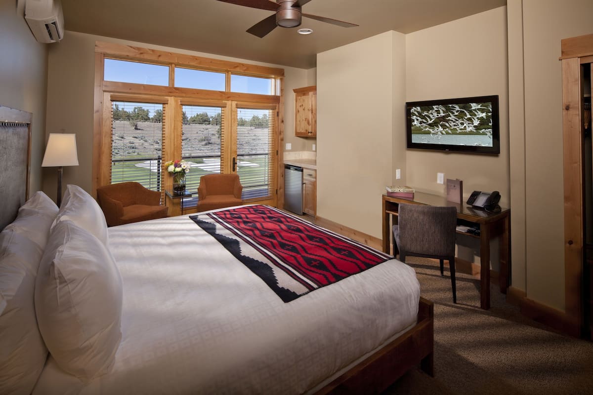 A bedroom with a large bed, a desk, a chair, a television, and a window with a view of a field.