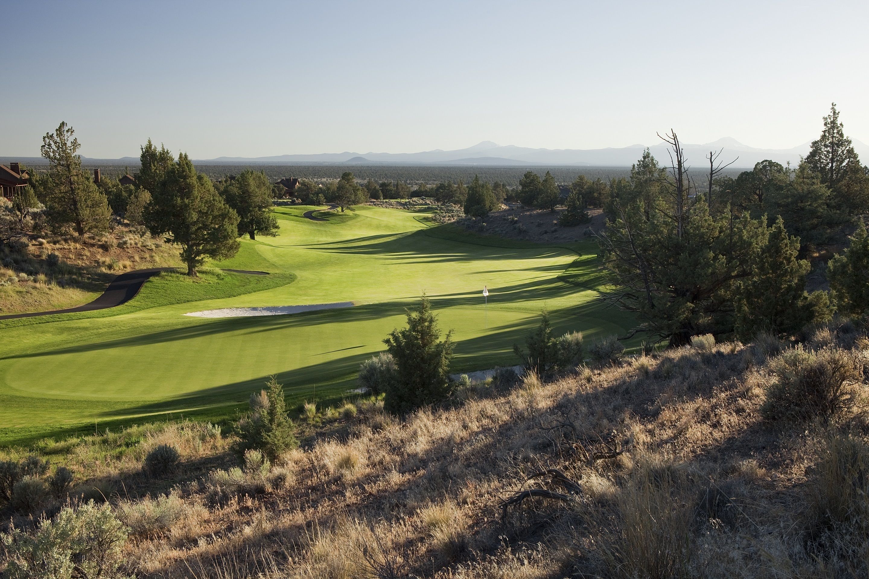 A golf course with a clear view of the green, fairways, and surrounding trees.