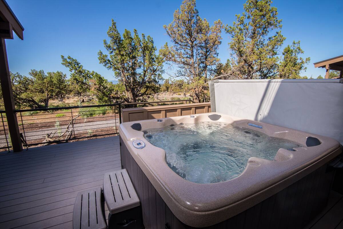 A hot tub on a wooden deck with a view of trees and a clear sky.