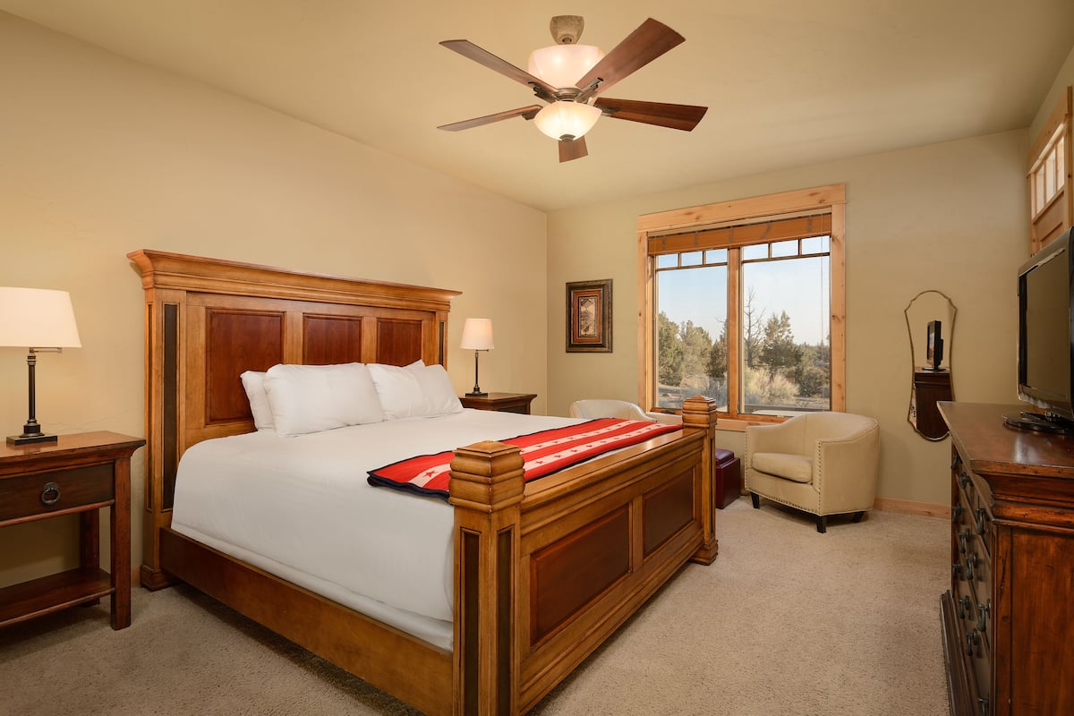 A bedroom with a wooden bed, a ceiling fan, a window with a view, a chair, and a dresser.