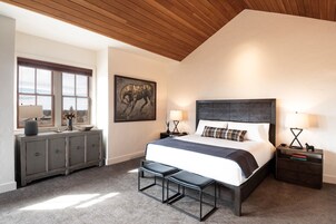 Camera da letto con un letto grande, soffitto in legno, finestra vista, una cassettiera e un quadro appeso al muro.
