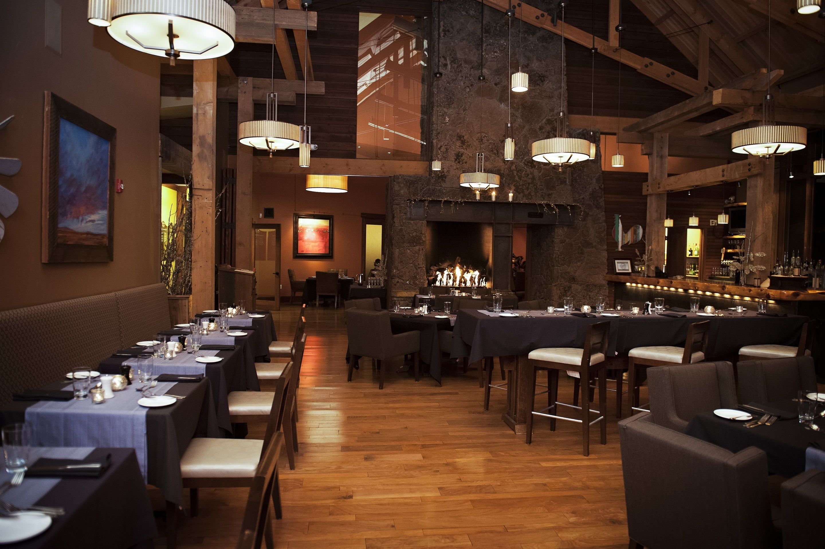 Un restaurant avec de longues tables, des luminaires suspendus et une cheminée.