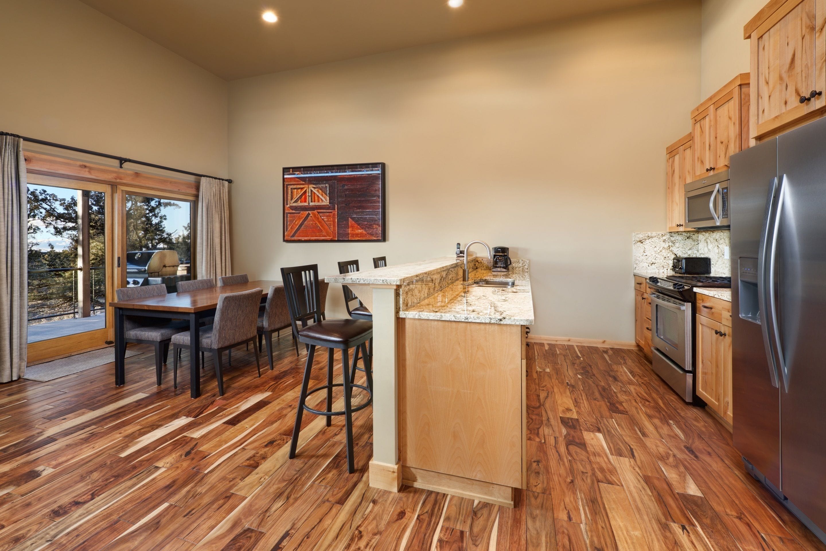 A modern kitchen with wooden flooring, a dining area with chairs, a kitchen island, and a refrigerator.