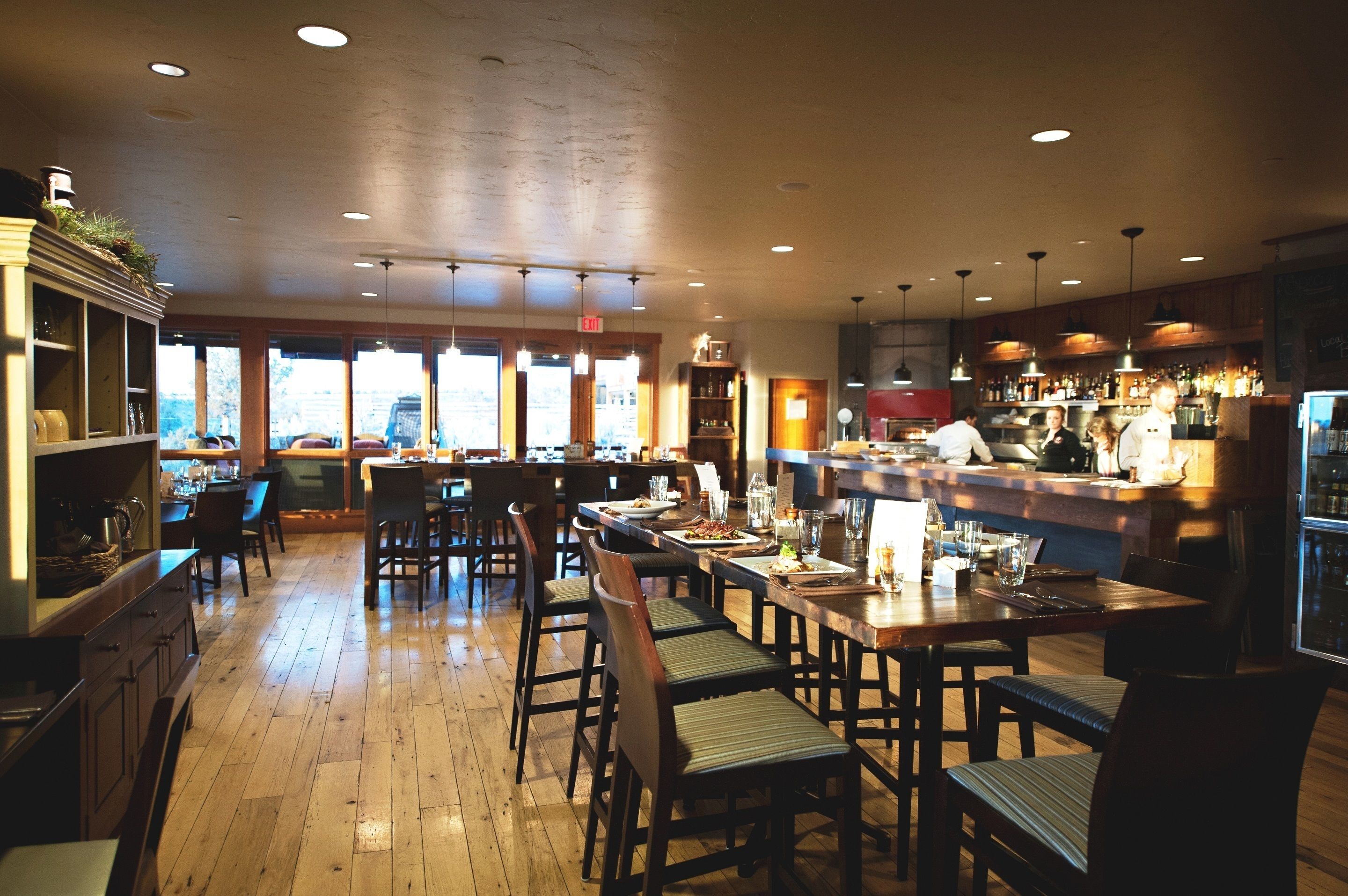Un restaurante con pisos de madera, varias mesas para comer y una zona de bar.