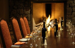 A long dining table set for a meal with chairs, wine bottles, glasses, and a fireplace in the background.