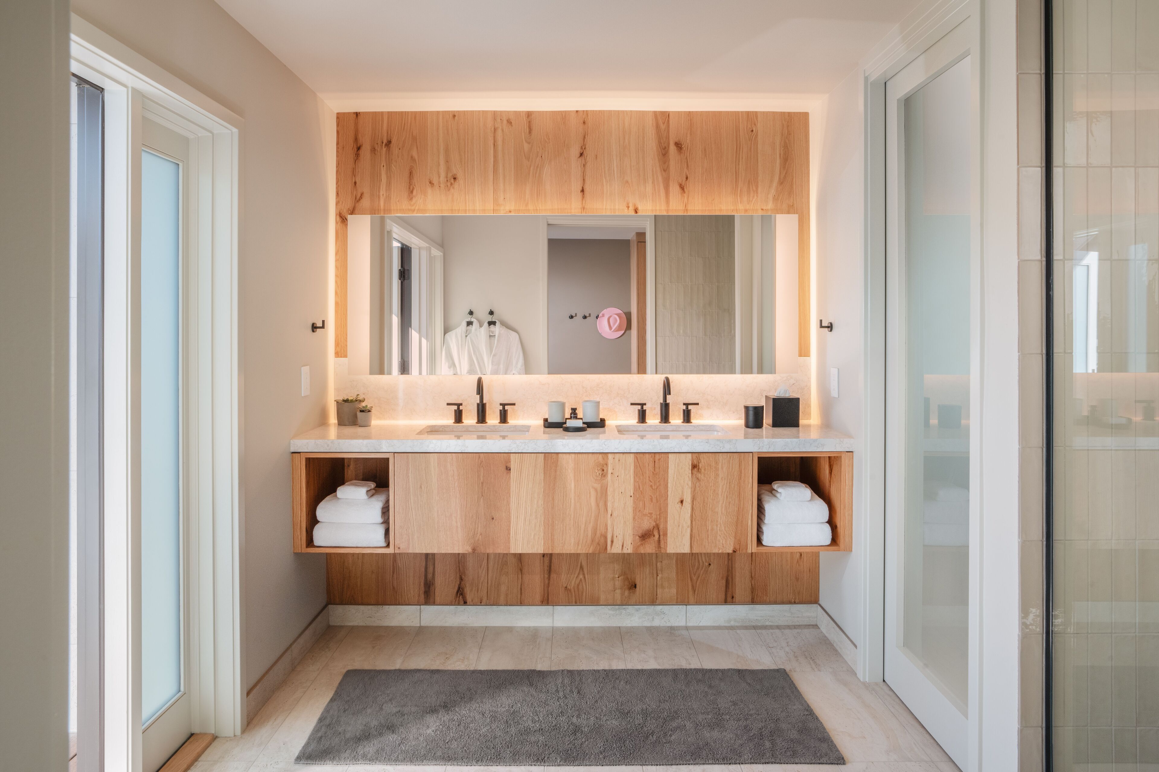 A modern bathroom with a wooden vanity, a large mirror, and a glass shower enclosure.