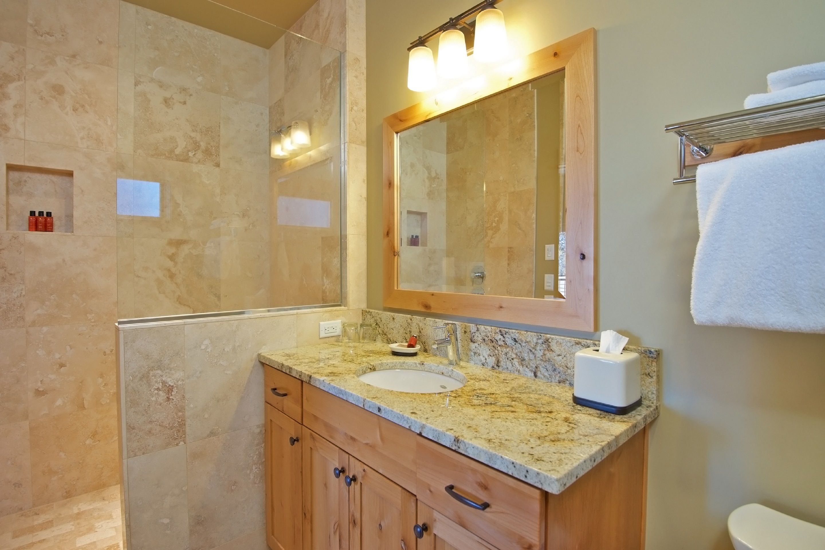 A bathroom with a granite countertop, a sink, a mirror, and a shower area.