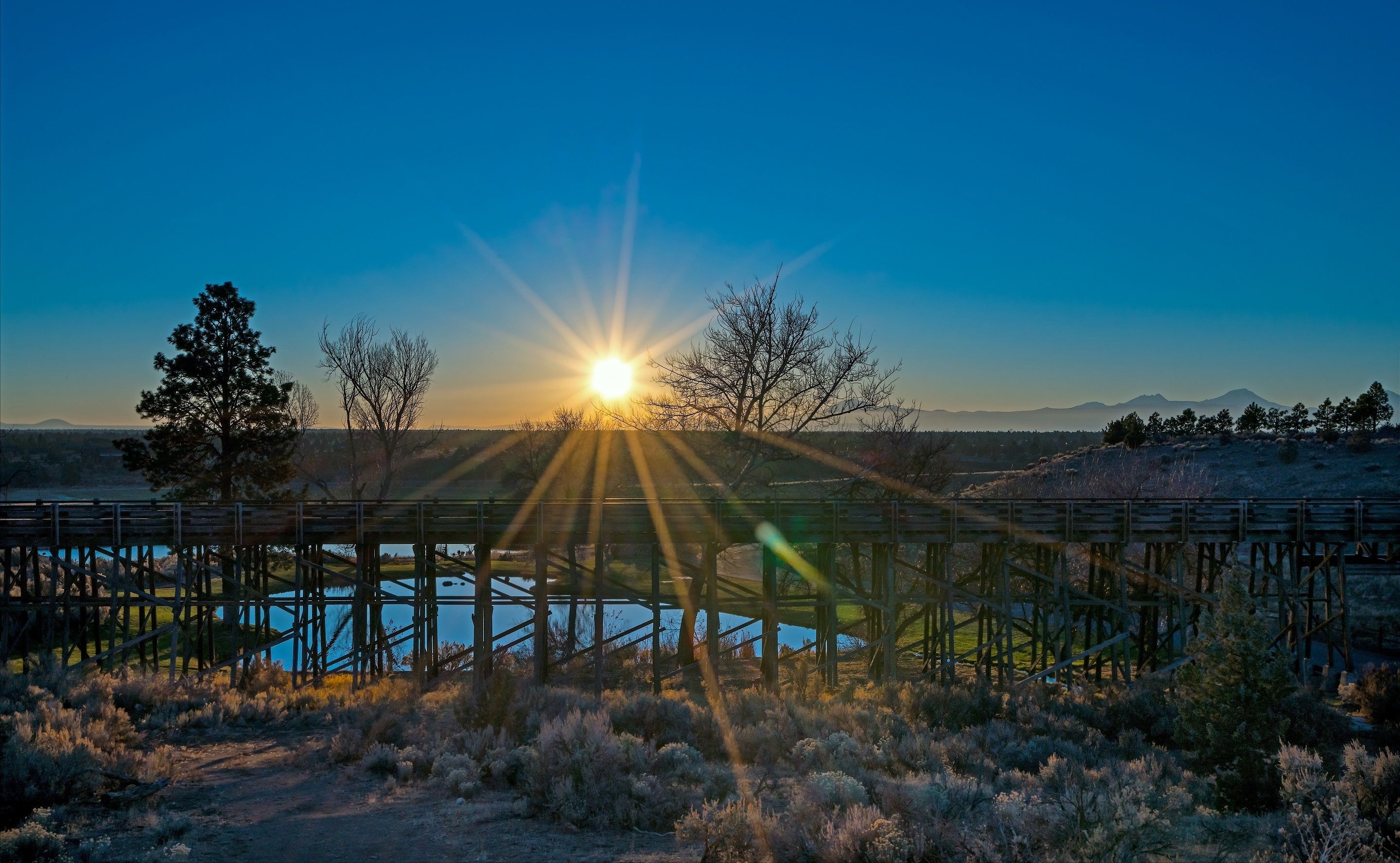 A wooden bridge over a body of water with a sunset in the background.