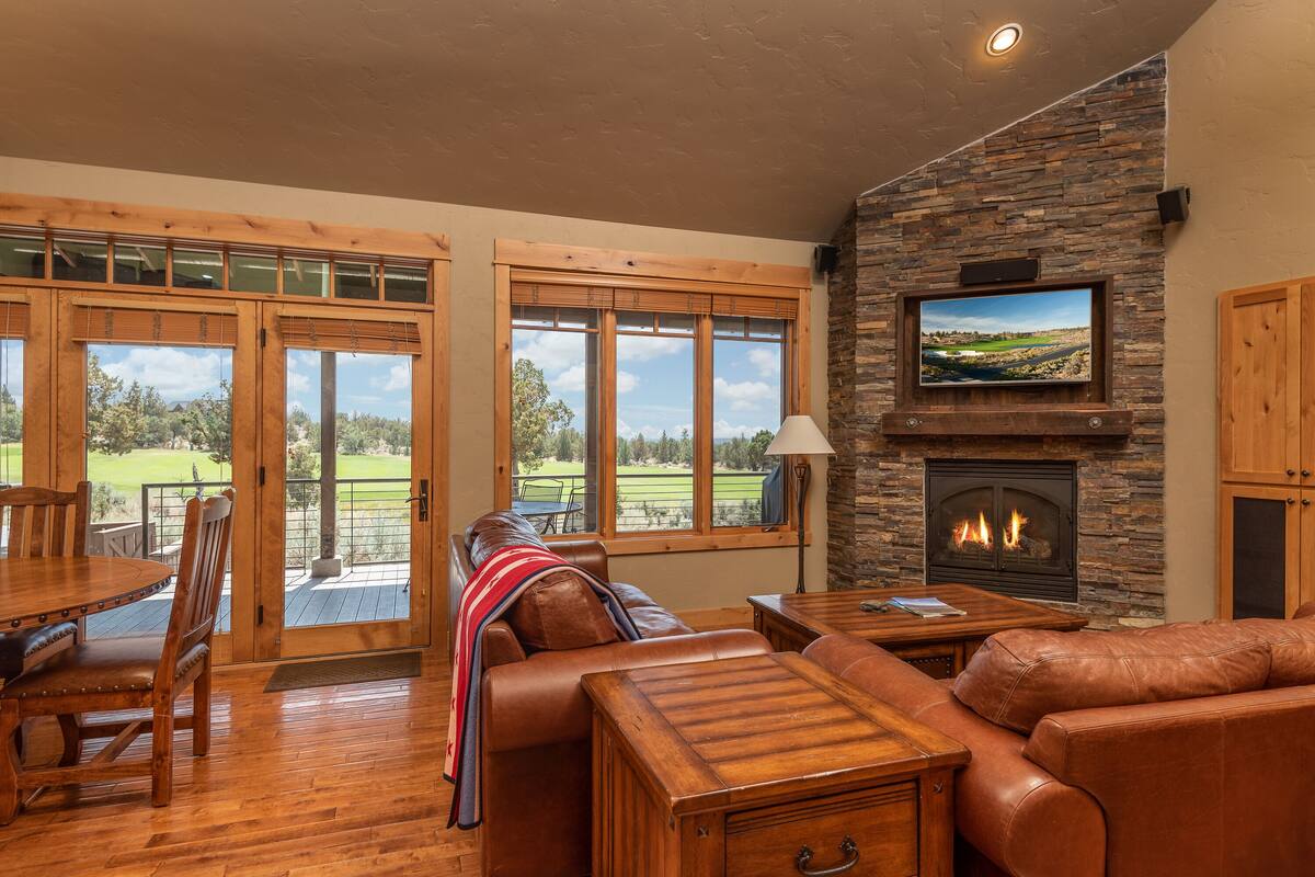 A spacious living room with a fireplace, leather furniture, and large windows offering a view of the outdoors.