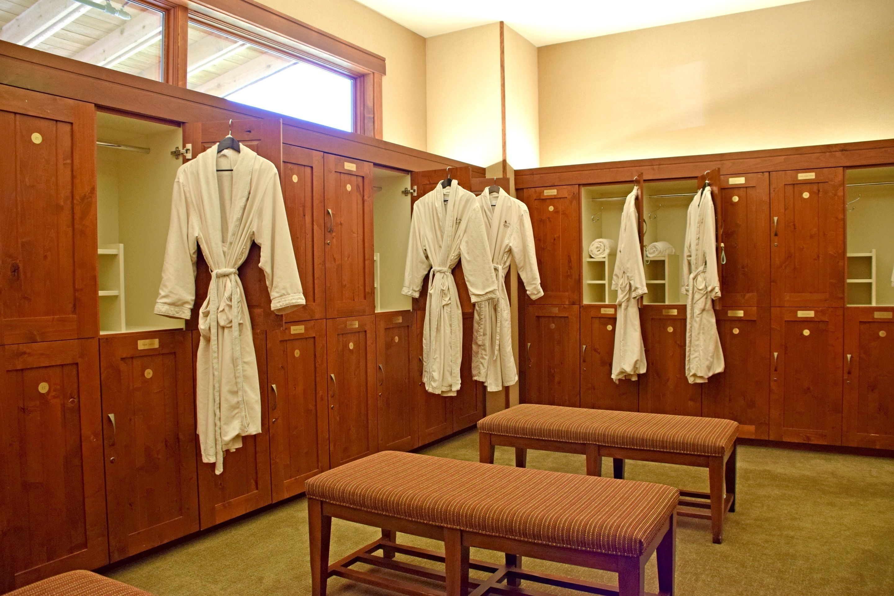 Habitación de hotel con armarios de madera, un banco y batas colgadas en ganchos.