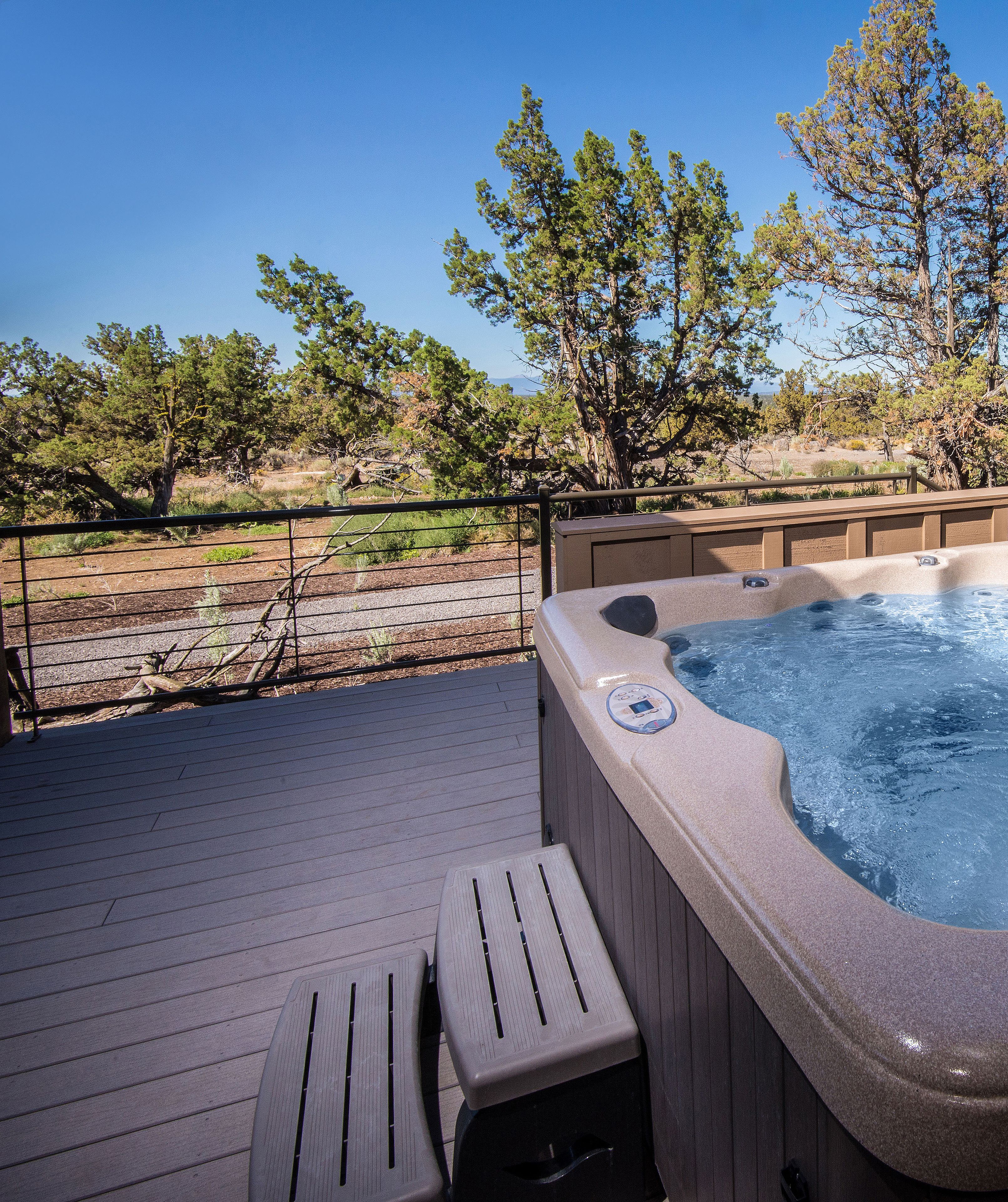 A hot tub on a wooden deck with a view of trees and a clear sky.