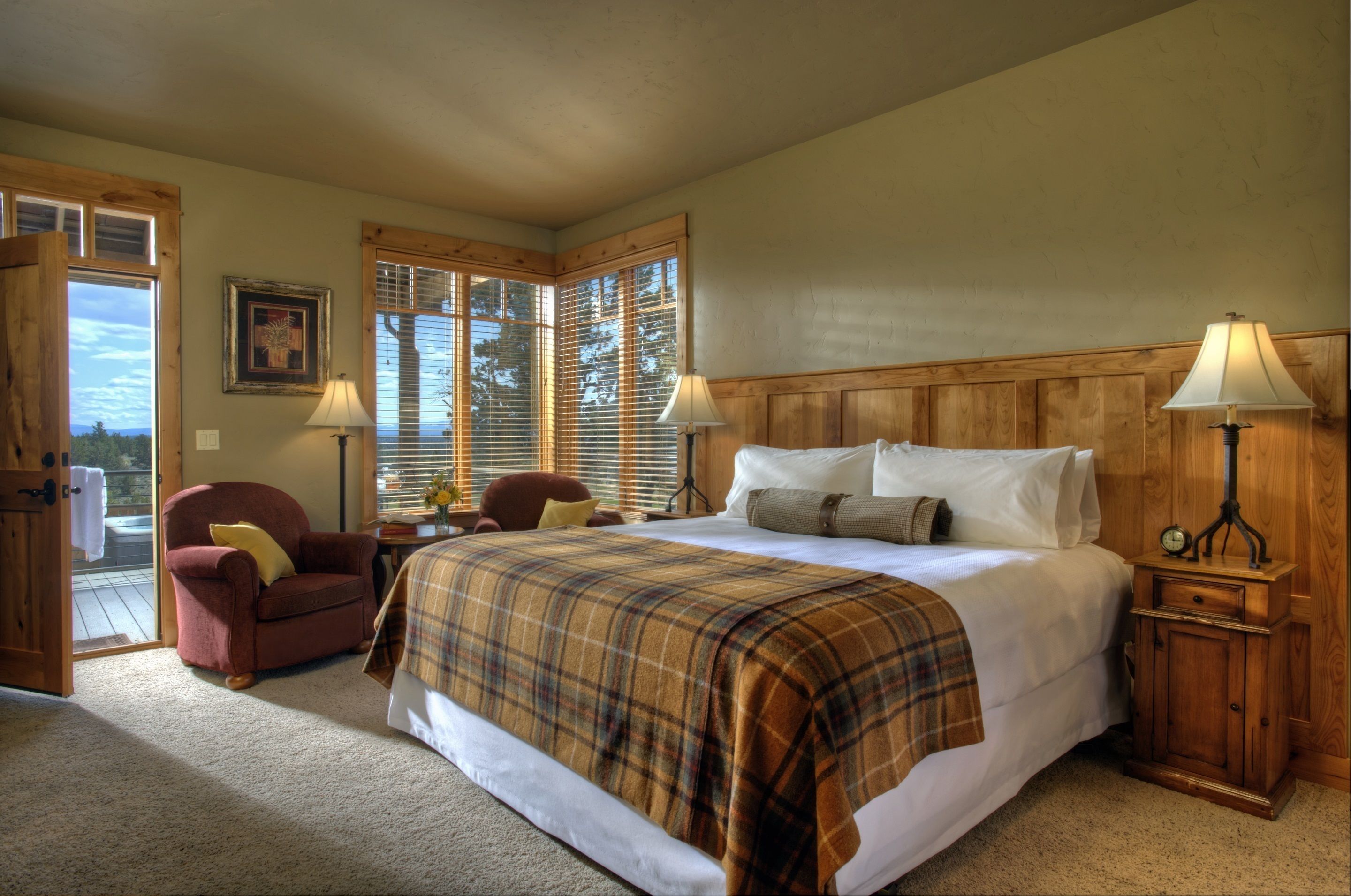 A bedroom with a large bed, two bedside tables with lamps, a chair, and a window with blinds.