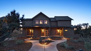 A modern two-story house with a symmetrical design, featuring a central entrance with steps, a covered porch, and a landscaped driveway.