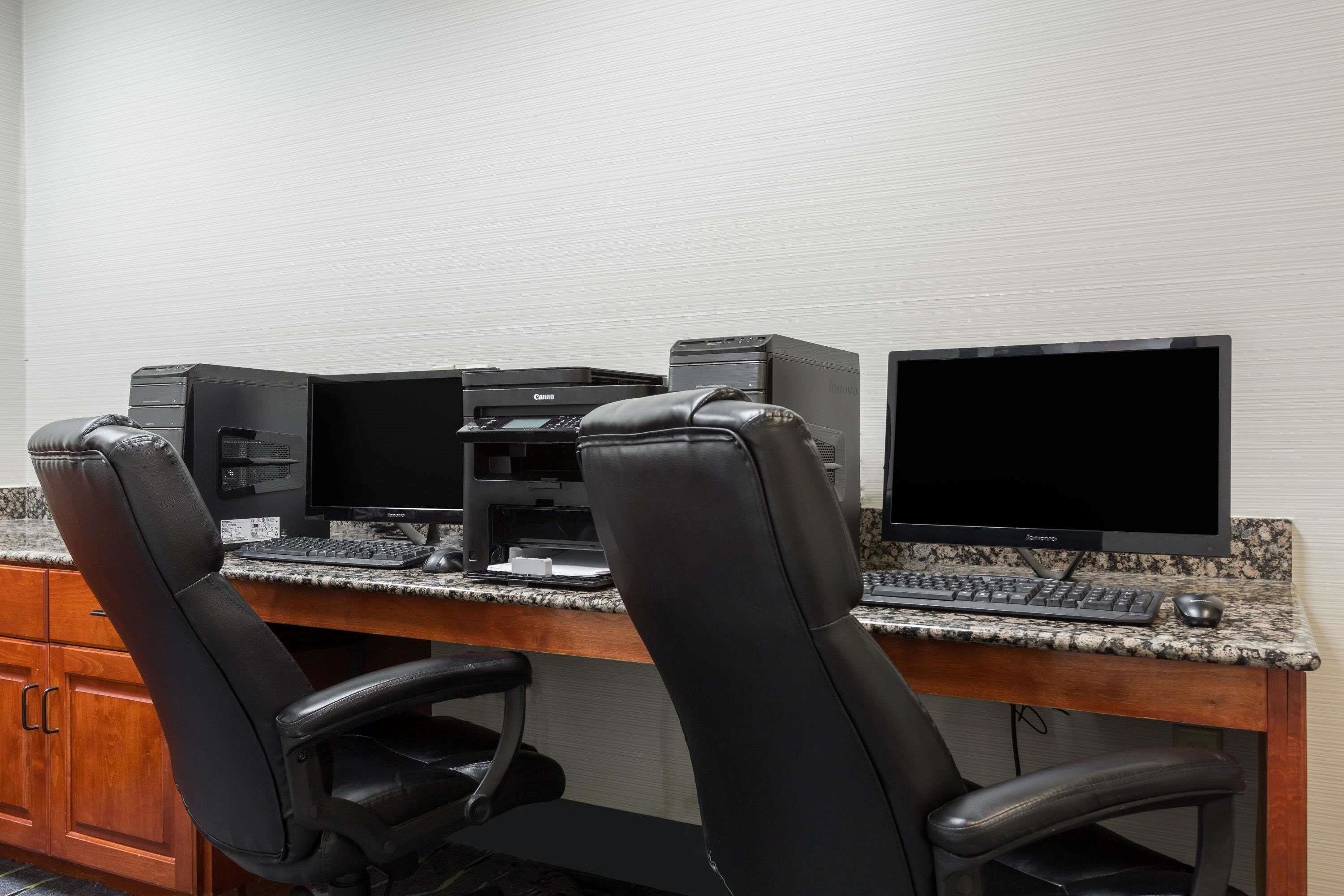 A workspace with two black office chairs, a desktop computer, and a monitor on a granite countertop.