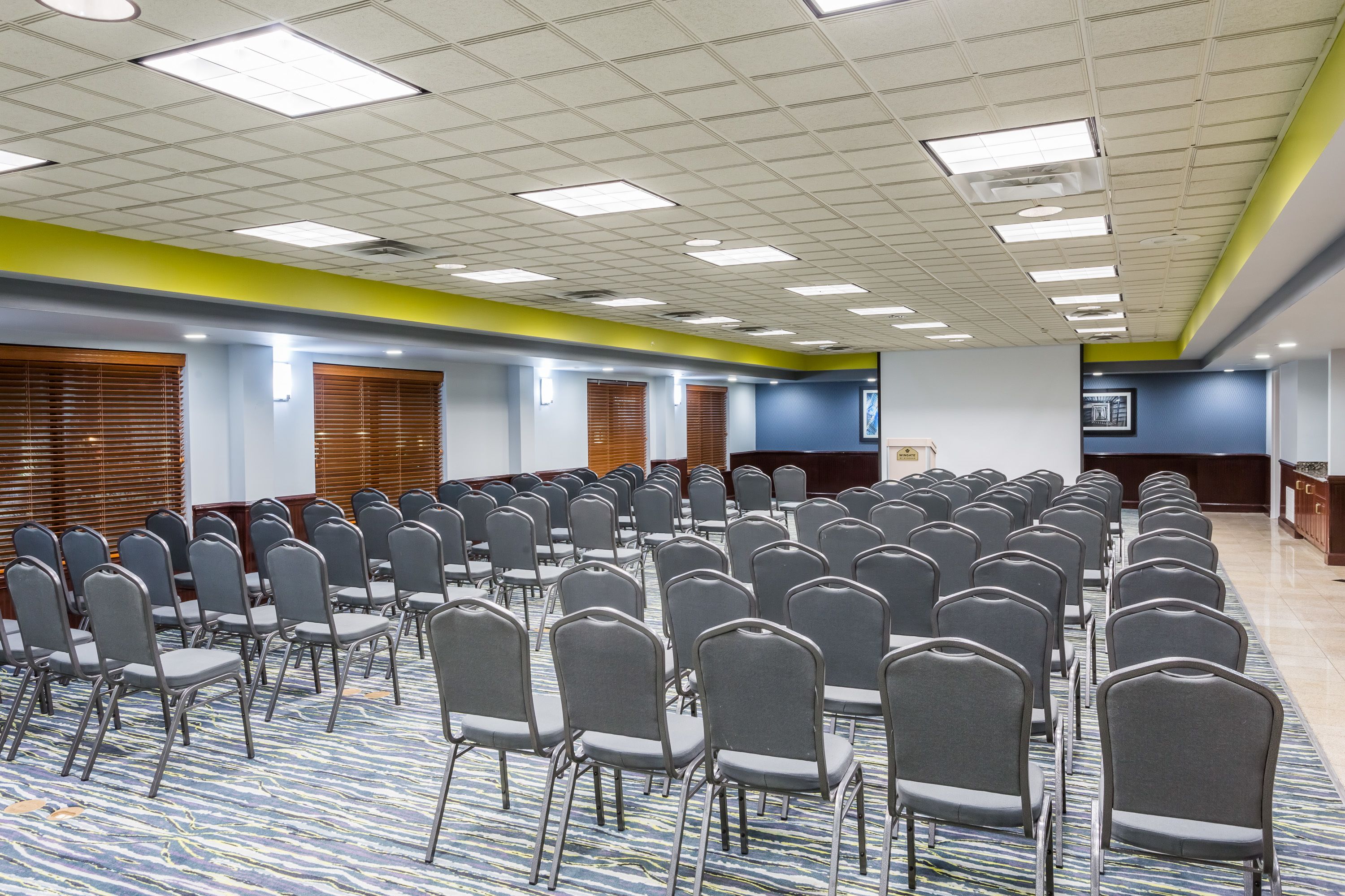 A conference room with rows of chairs, a patterned carpet, and a ceiling with fluorescent lights.