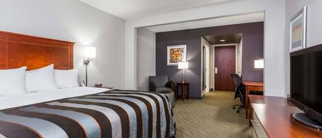 A hotel room with a large bed, a desk, a television, and a chair.
