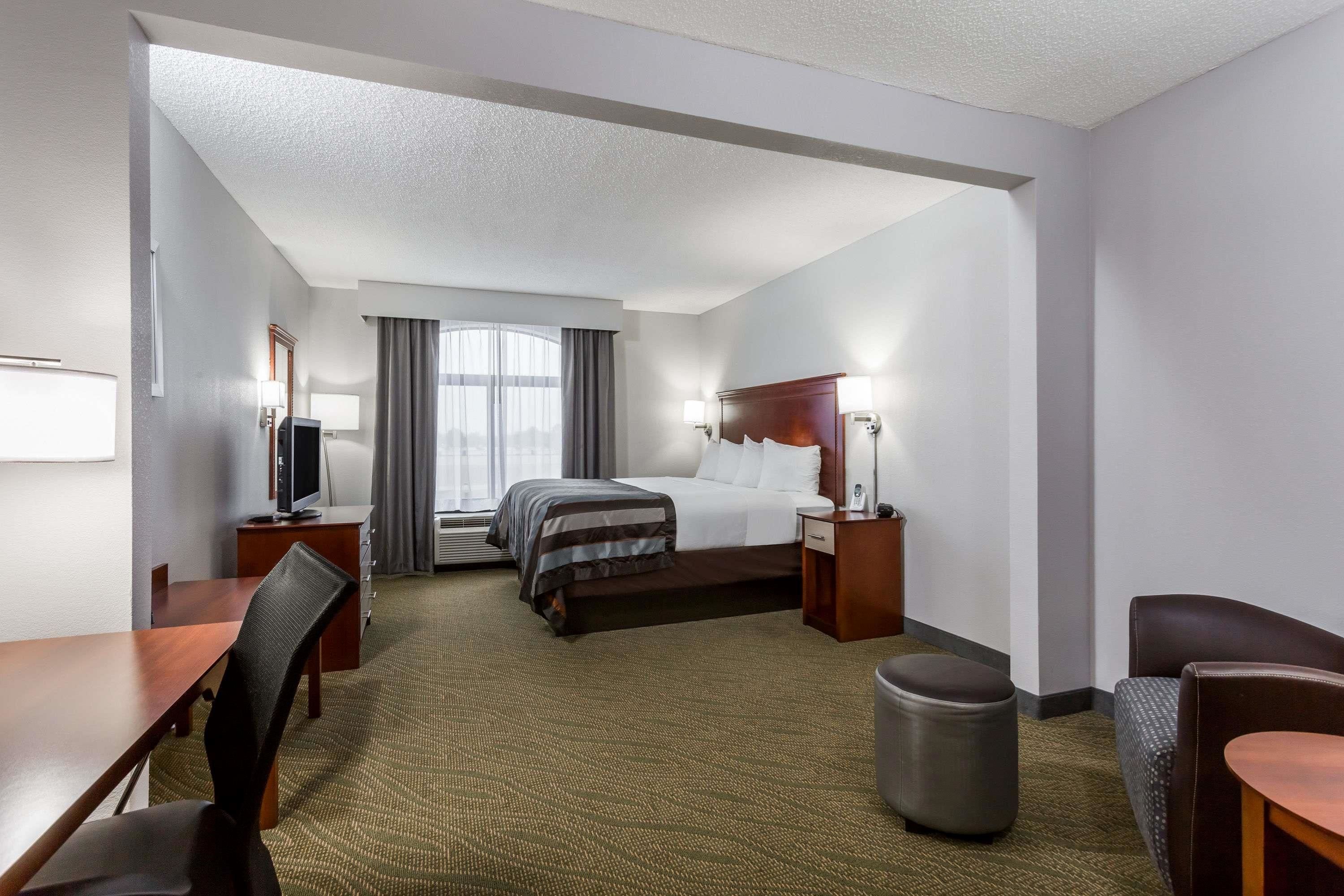 A hotel room with a bed, a desk, a chair, a trash bin, and a window with curtains.