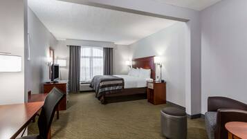 A hotel room with a bed, a desk, a chair, a trash bin, and a window with curtains.