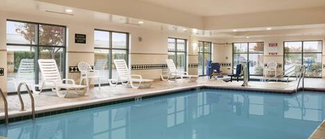 A swimming pool with white lounge chairs and a view of the outdoors.
