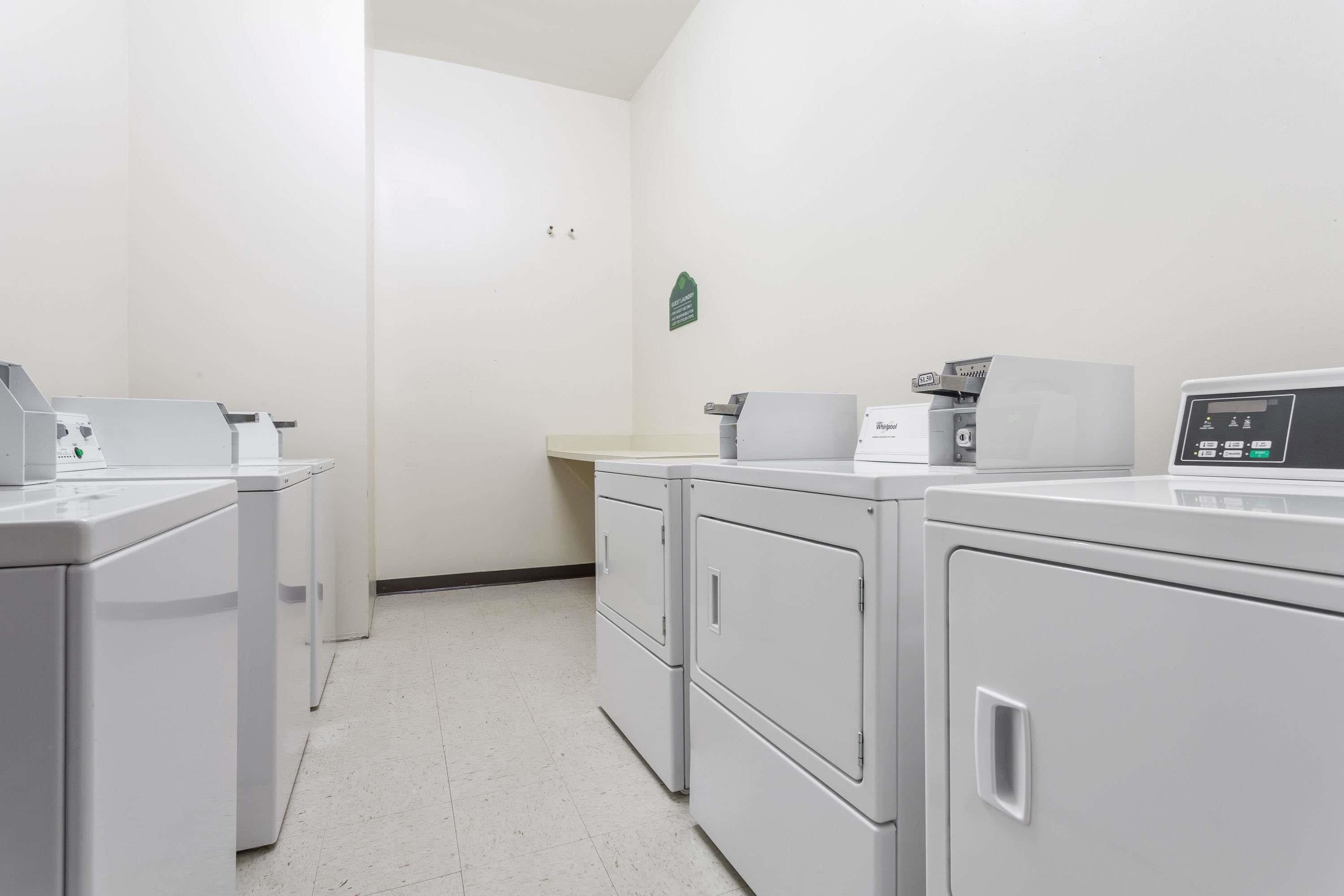 A laundry facility with multiple washing machines and dryers, a countertop with a scale, and a wall-mounted sign.