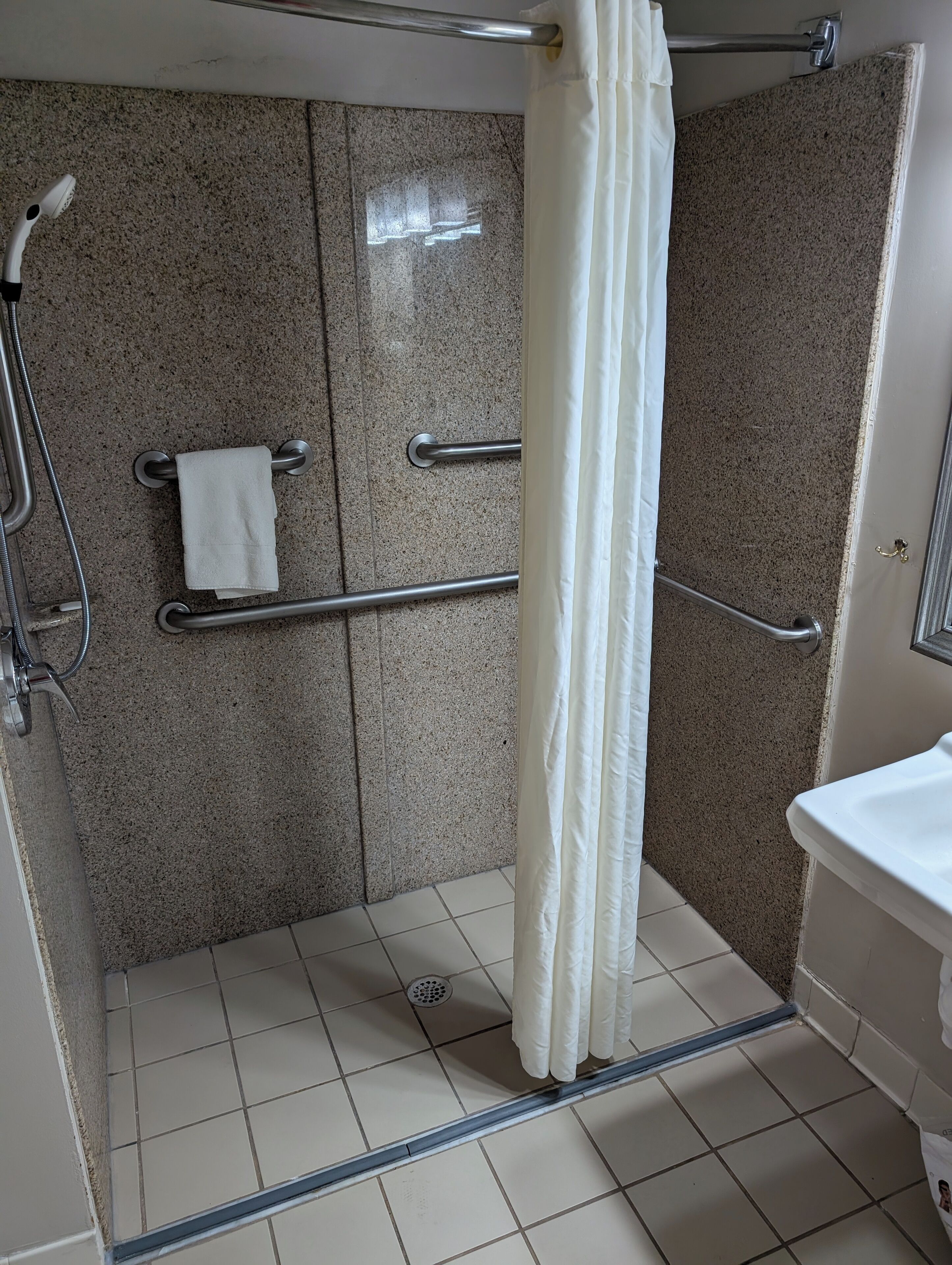 A shower area with a grab bar, a towel rack, and a shower curtain.
