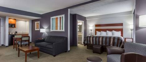 A hotel room with a bed, two sofas, a dining table, and a small kitchen area.