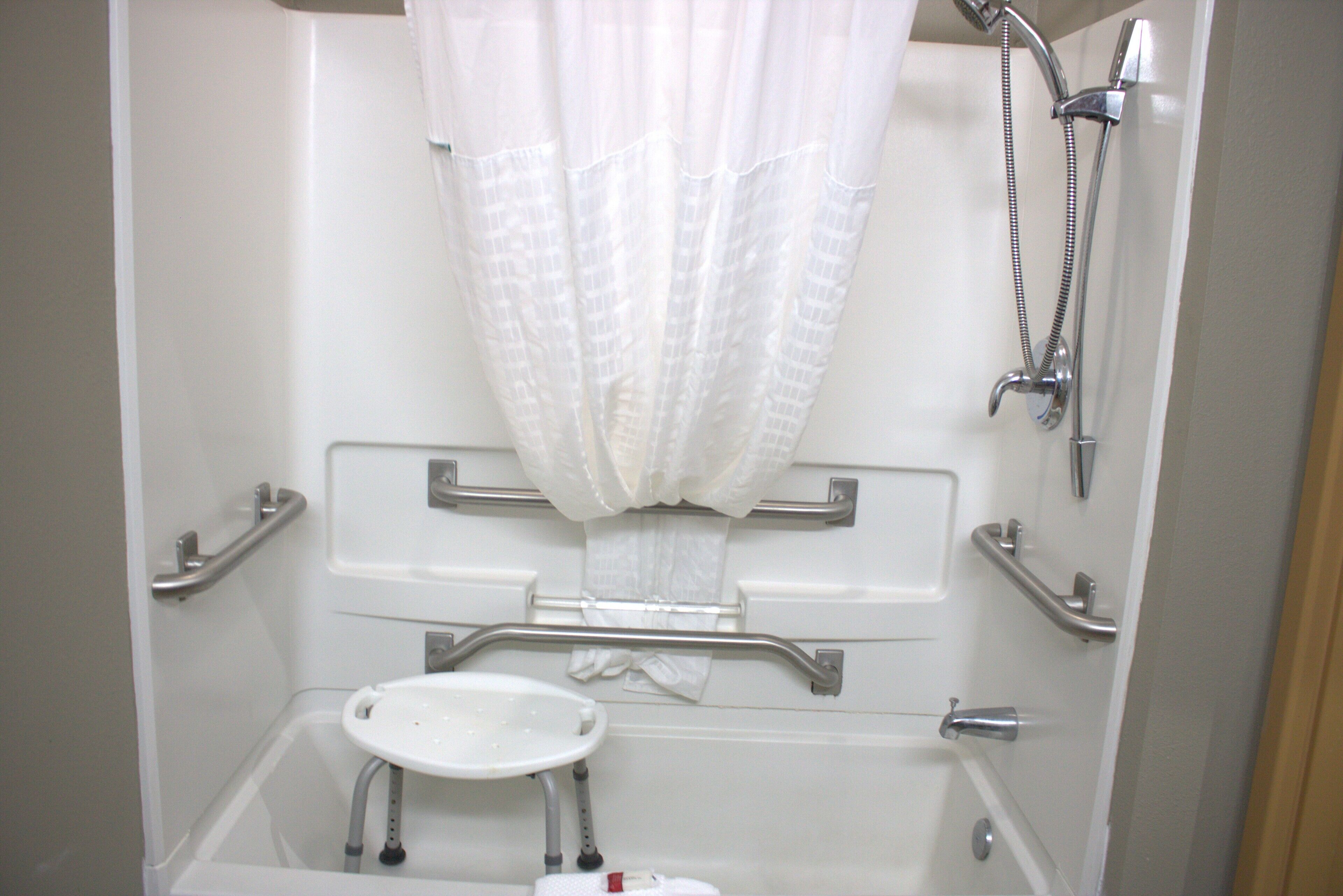 Baño con ducha, barras de apoyo, un lavamanos pequeño y un inodoro.